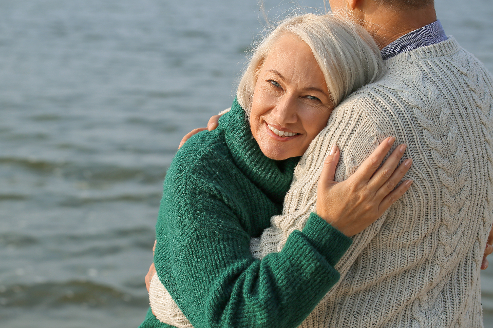 Smiling woman embracing her partner outdoors by the water
