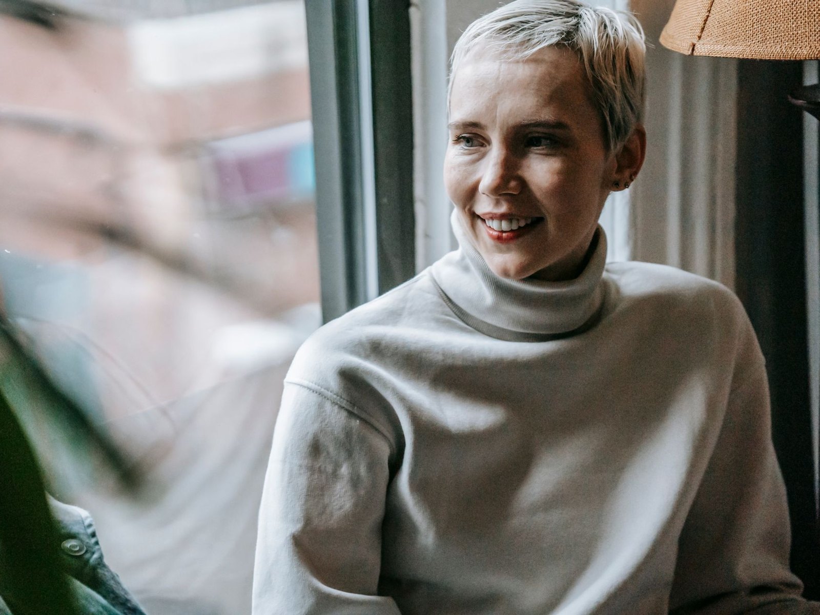Woman in a cream turtleneck smiling by a window